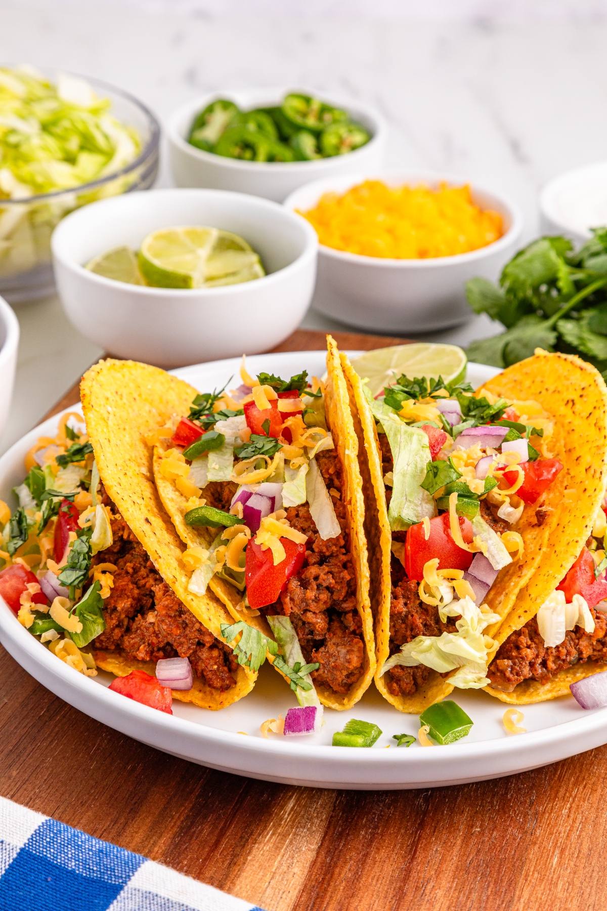Three hard shell slow cooker tacos filled with seasoned ground beef, lettuce, tomatoes, cheese, and onions on a white plate.