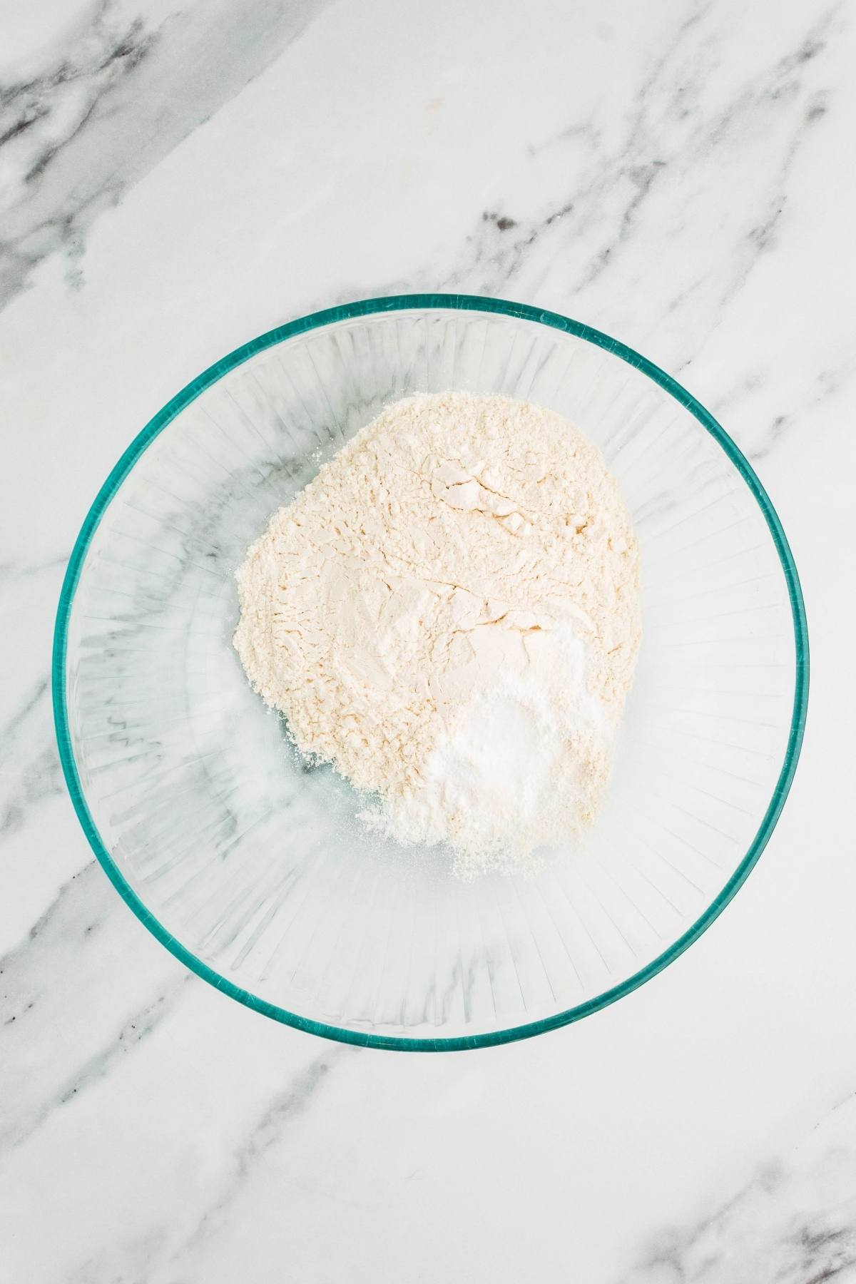 A glass bowl with flour and baking powder on a white marble surface.