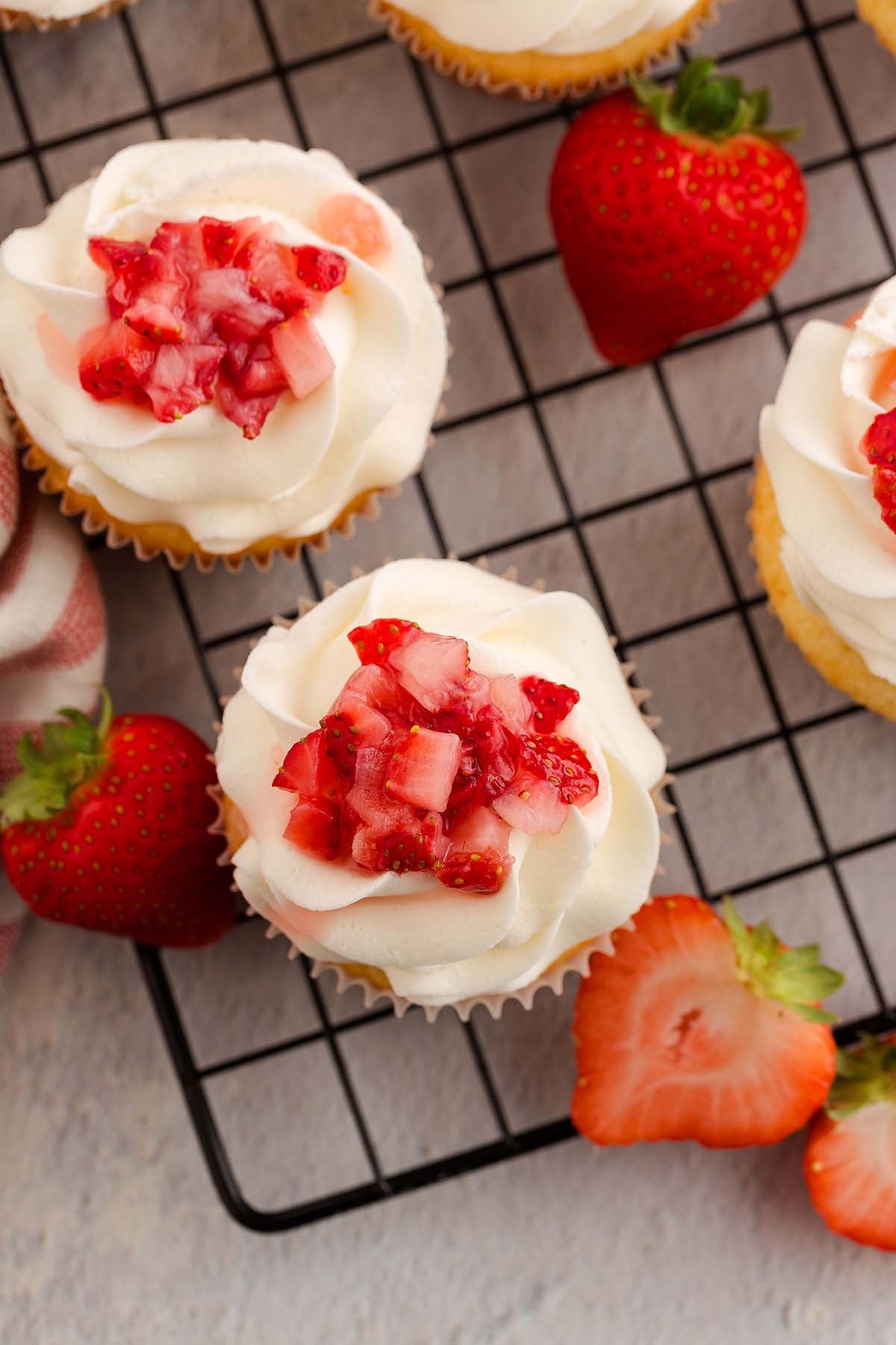 Strawberry Shortcake Cupcakes with vanilla cake, white frosting, and chopped strawberries on top, placed on a cooling rack.