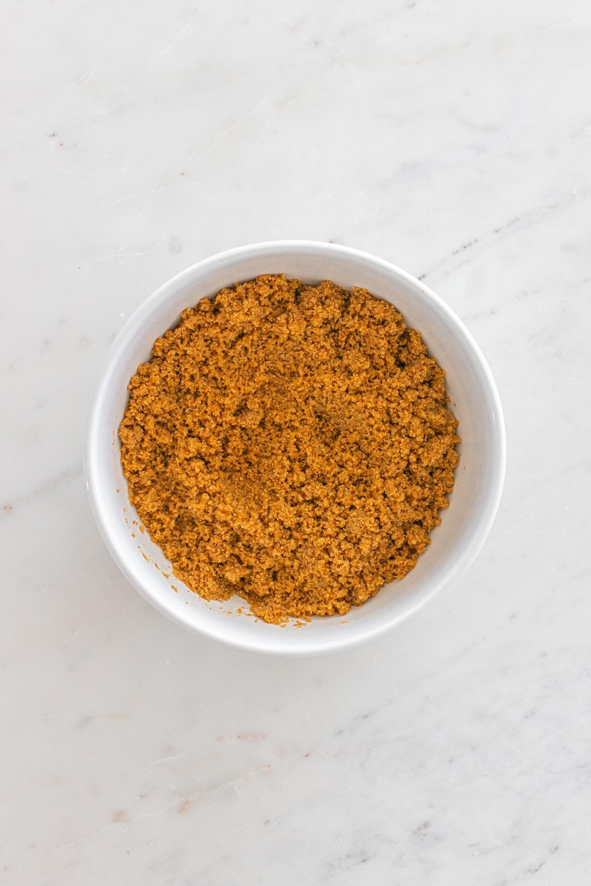 White bowl filled with ground brownish-orange spice on a light marble surface.