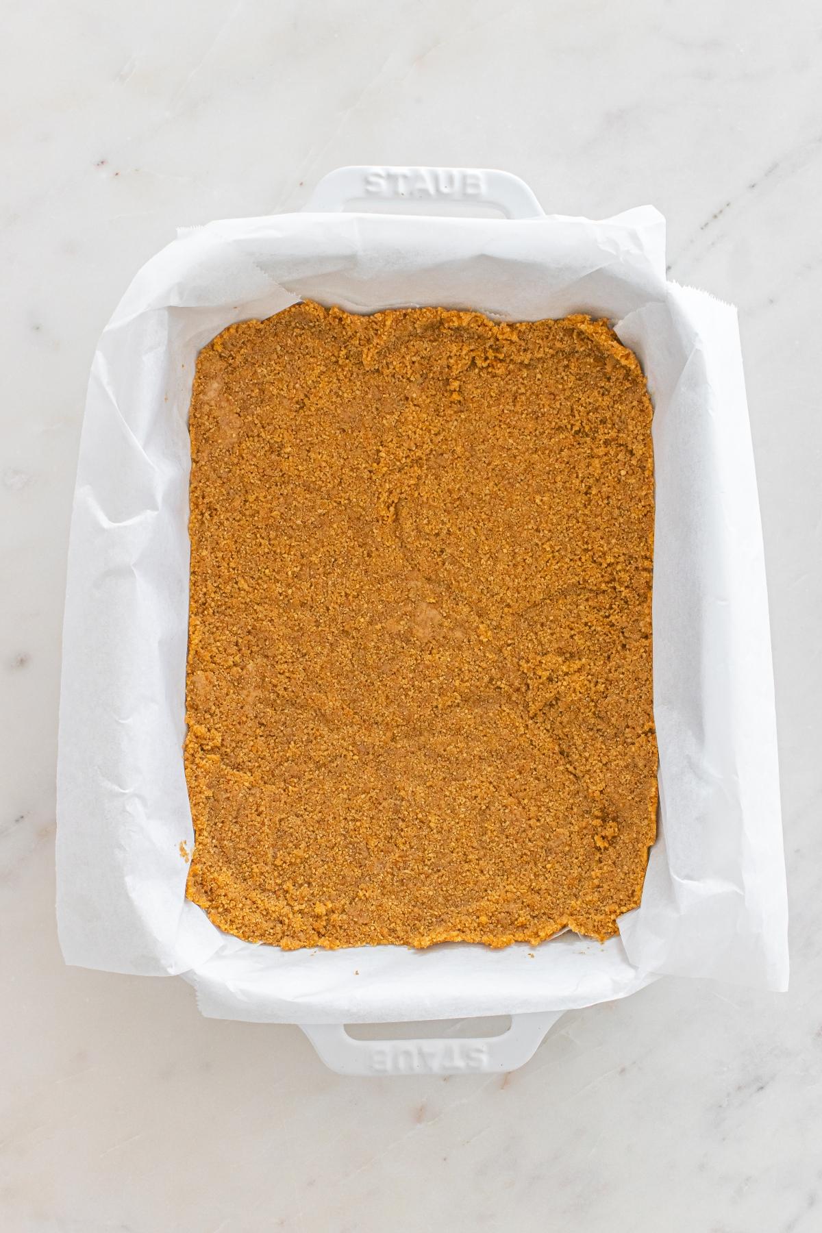 A parchment-lined baking dish with an even layer of brown crumb crust on a white marble surface.
