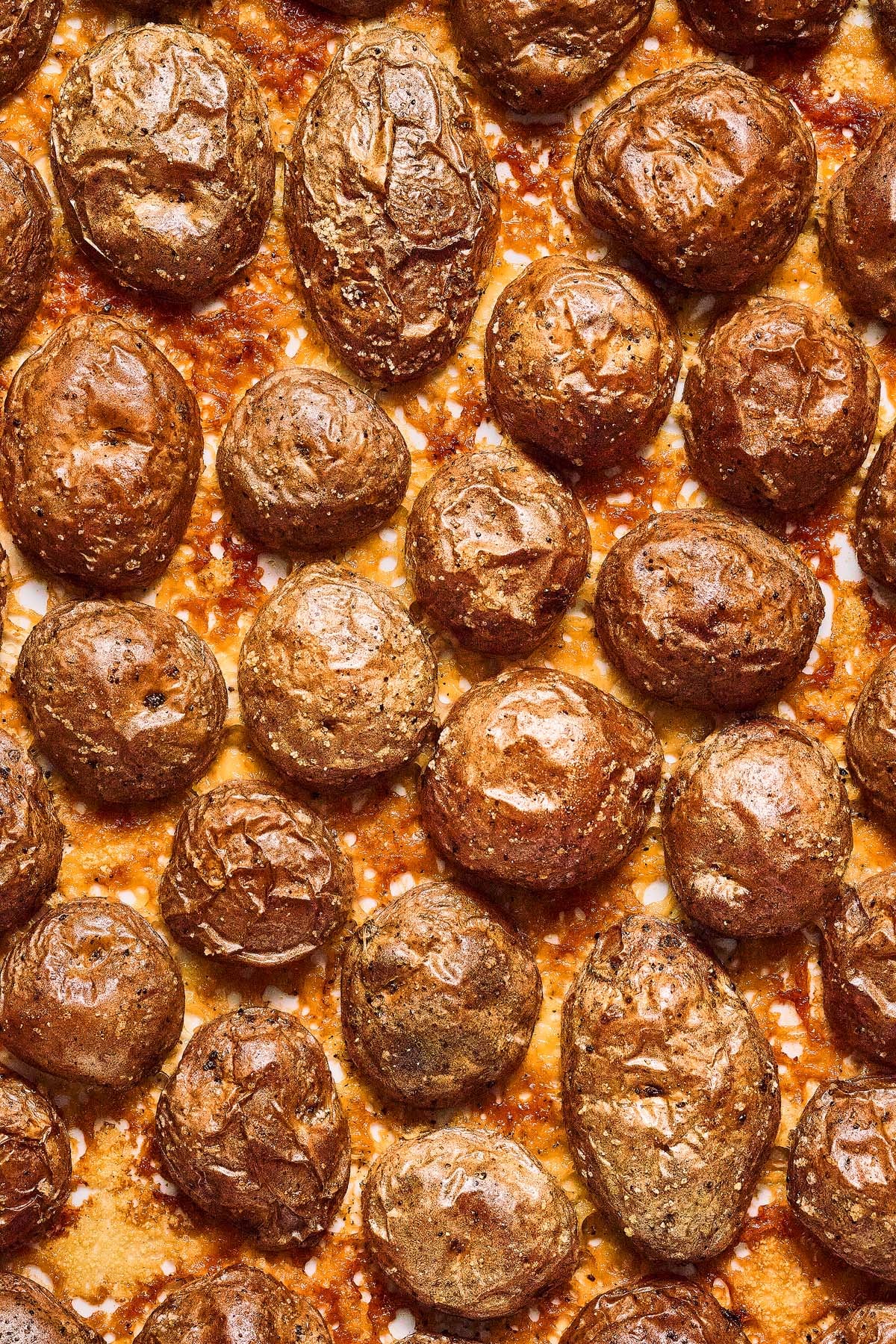 Golden brown roasted baby potatoes arranged closely together on a crispy, cheesy surface&mdash;these are the irresistible Crispy Parmesan Potatoes you won't want to miss.