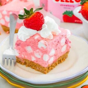 A slice of pink strawberry chiffon squares dessert with a graham crust, marshmallows, and a fresh strawberry on top.