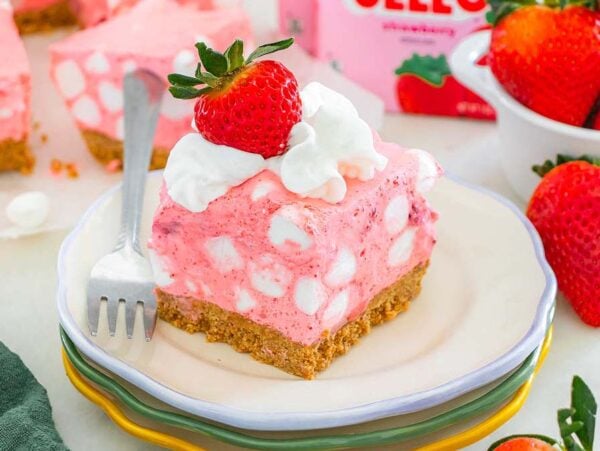 A slice of pink strawberry chiffon squares dessert with a graham crust, marshmallows, and a fresh strawberry on top.