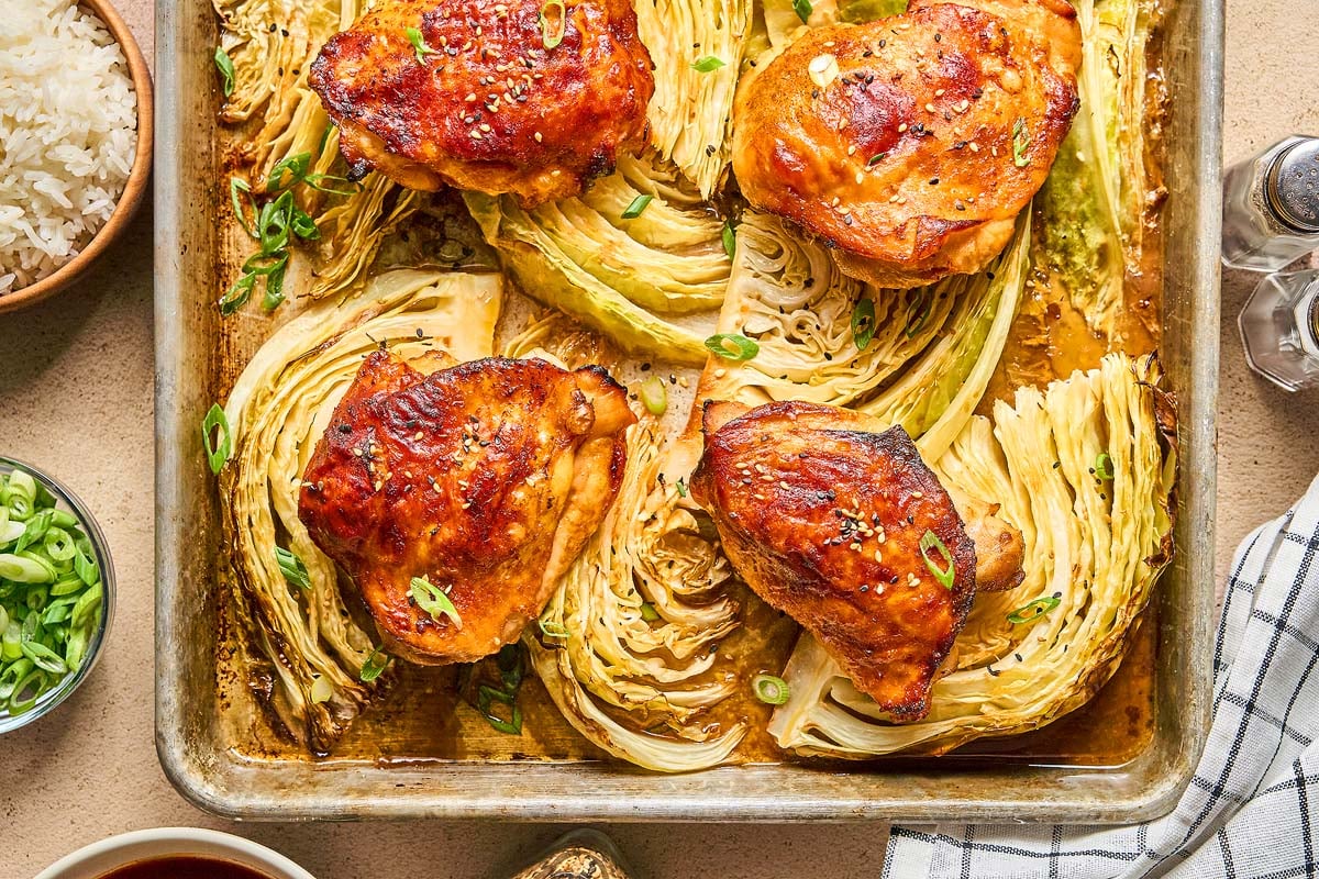 Sheet Pan Gochujang Chicken and Cabbage features roasted chicken thighs and cabbage wedges on a baking sheet, garnished with sliced green onions.