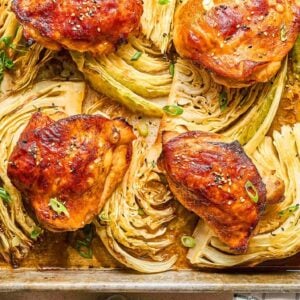 Sheet Pan Gochujang Chicken and Cabbage features roasted chicken thighs and cabbage wedges on a baking sheet, garnished with green onions and sesame seeds.