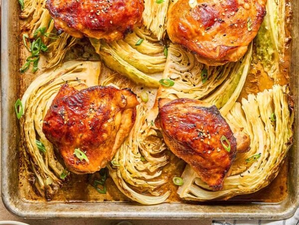 Sheet Pan Gochujang Chicken and Cabbage features roasted chicken thighs and cabbage wedges on a baking sheet, garnished with green onions and sesame seeds.
