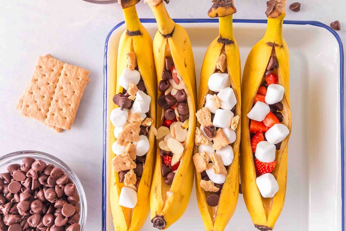 Four bananas split open and filled with marshmallows, chocolate chips, strawberries, and graham cracker pieces.