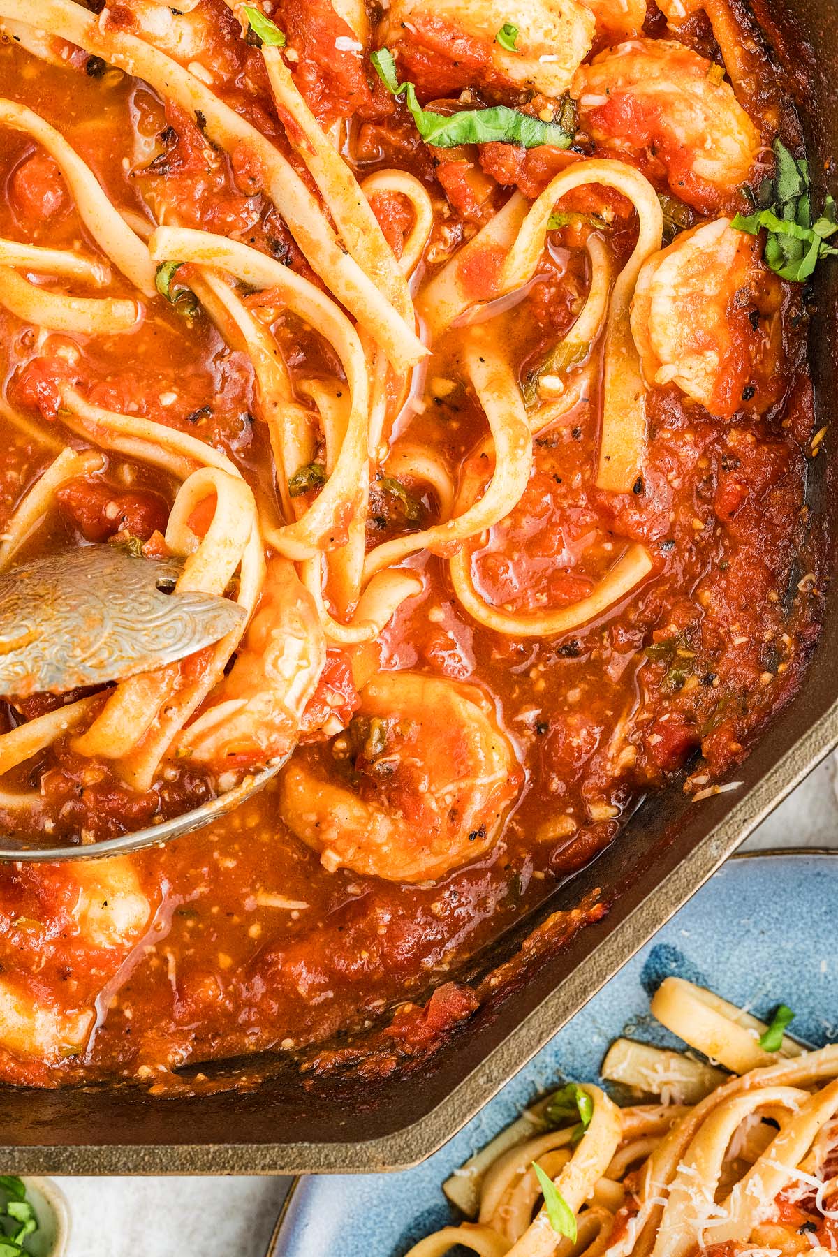 Top view of Shrimp fra Diavolo fettuccine pasta in tomato sauce, garnished with herbs, served in a skillet with a serving spoon.