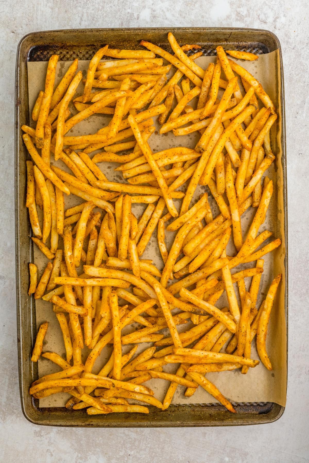 A baking sheet lined with parchment paper, covered with seasoned, cooked French fries.