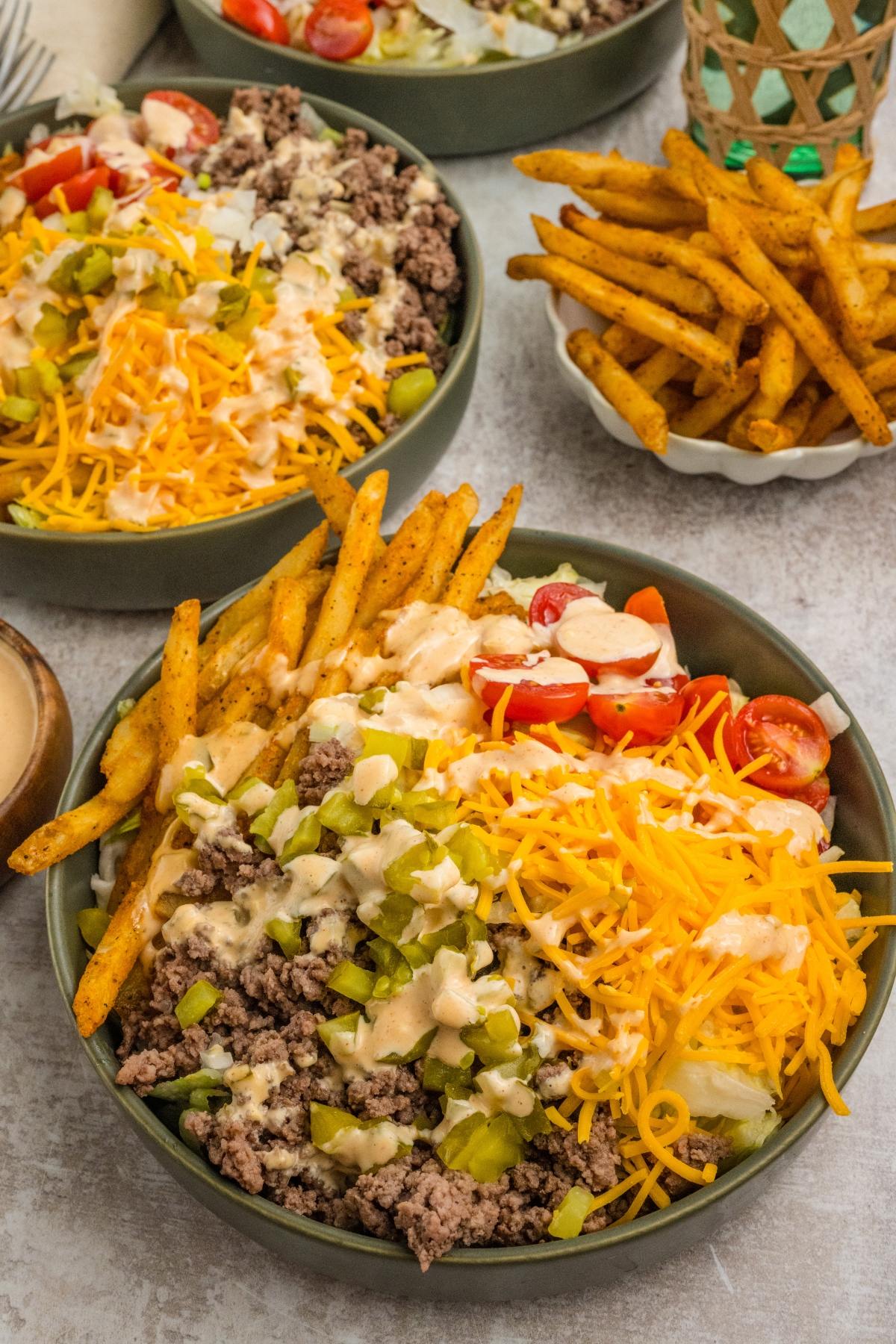 Bowls of big mac salad topped with ground beef, shredded cheese, fries, tomatoes, pickles, and creamy dressing.