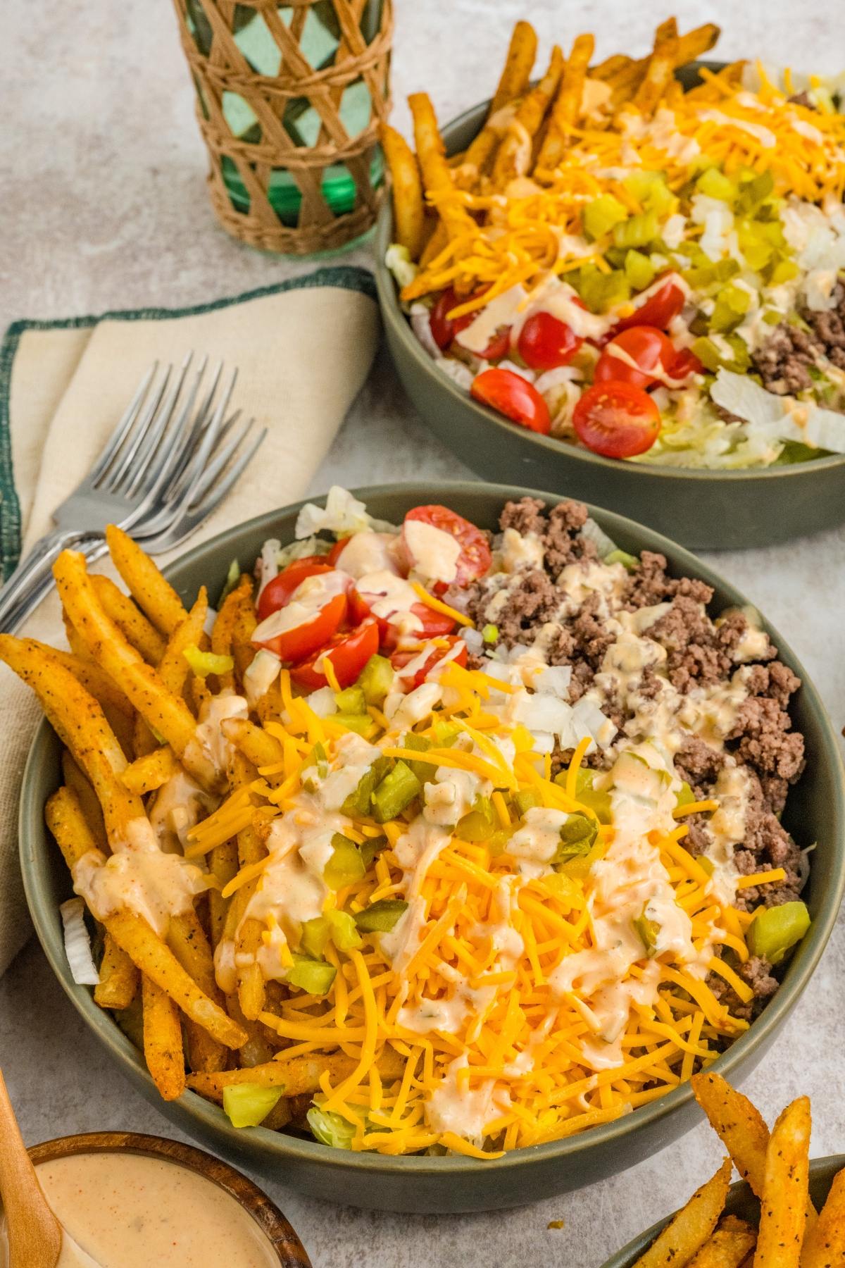 Two bowls big mac salad with seasoned fries, ground beef, shredded cheese, lettuce, tomatoes, pickles, and creamy sauce.