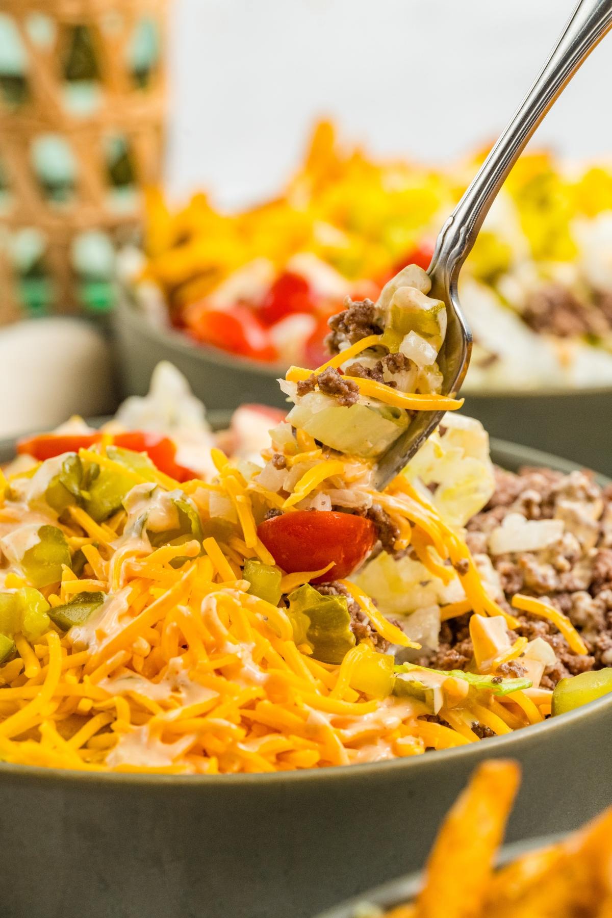A fork lifts a bite of big mac salad with ground beef, shredded cheese, lettuce, tomatoes, and pickles.