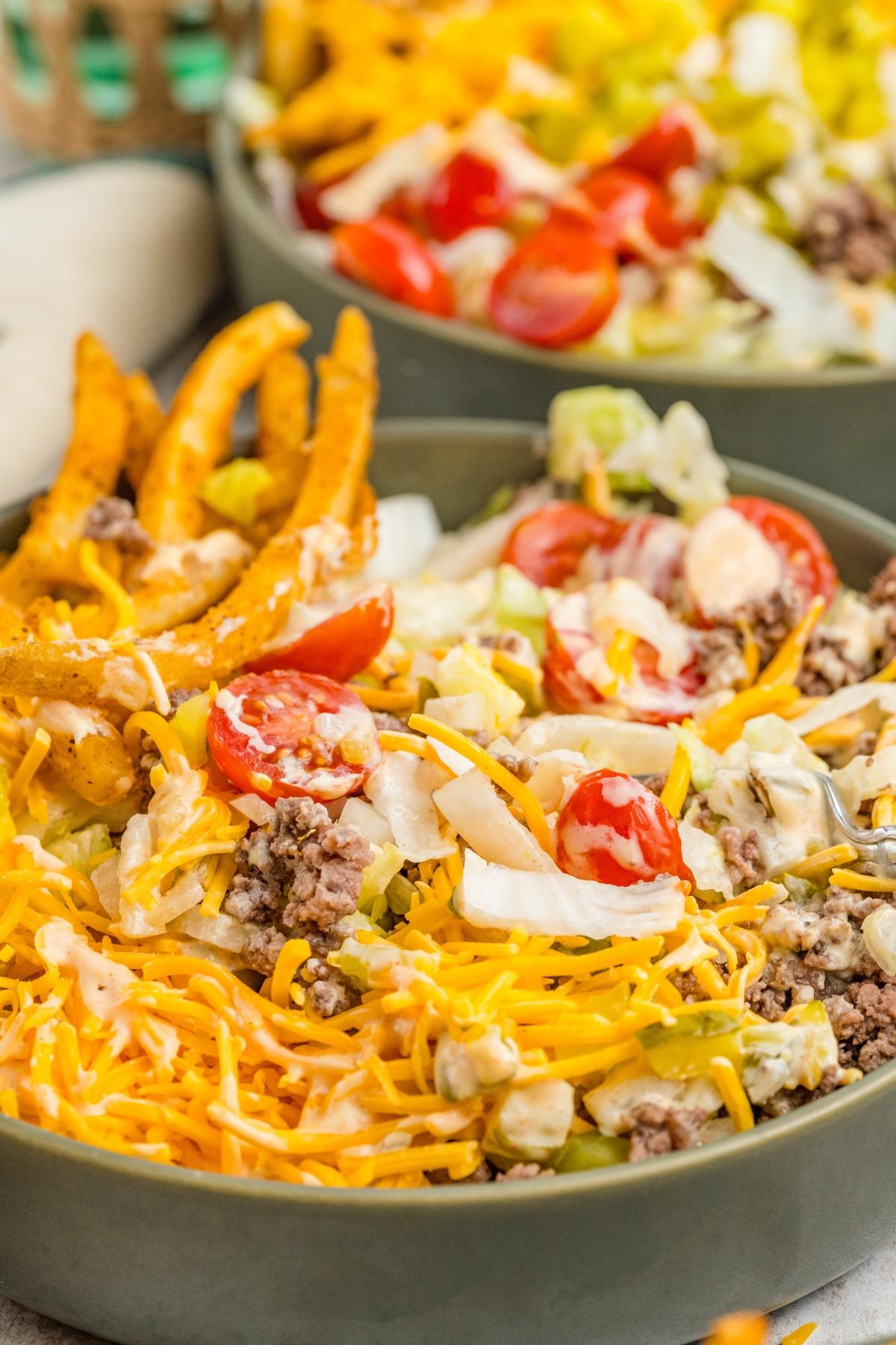 A bowl of big mac salad with ground beef, shredded cheese, tomatoes, and crinkle fries on top.