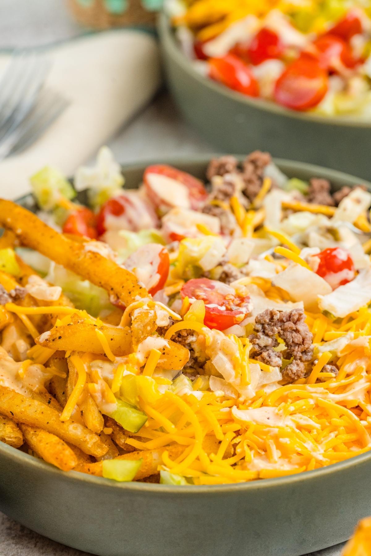 A bowl of big mac salad with ground beef, shredded cheese, fries, lettuce, tomatoes, and dressing.