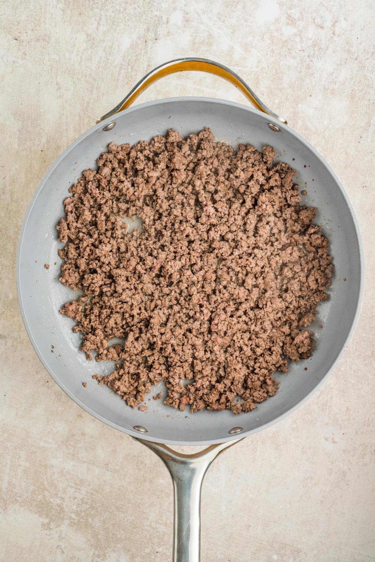 Cooked ground beef in a gray skillet on a light-colored surface, viewed from above.