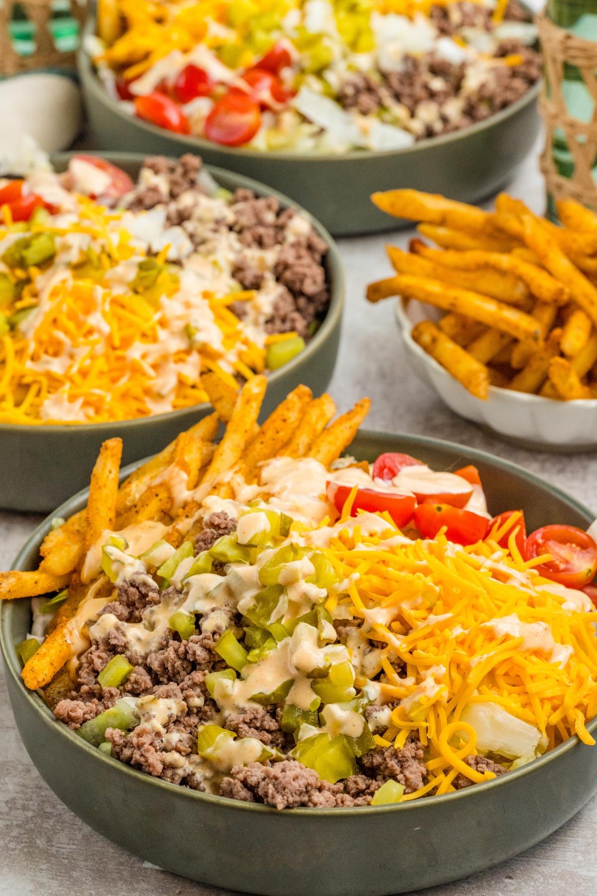 Bowls of big mac salad with ground beef, shredded cheese, fries, pickles, tomatoes, and creamy dressing.