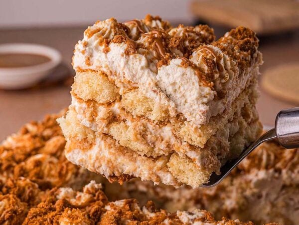 A close-up of a creamy Biscoff Tiramisu slice being lifted from a tray with a spatula, showcasing its luscious layers.