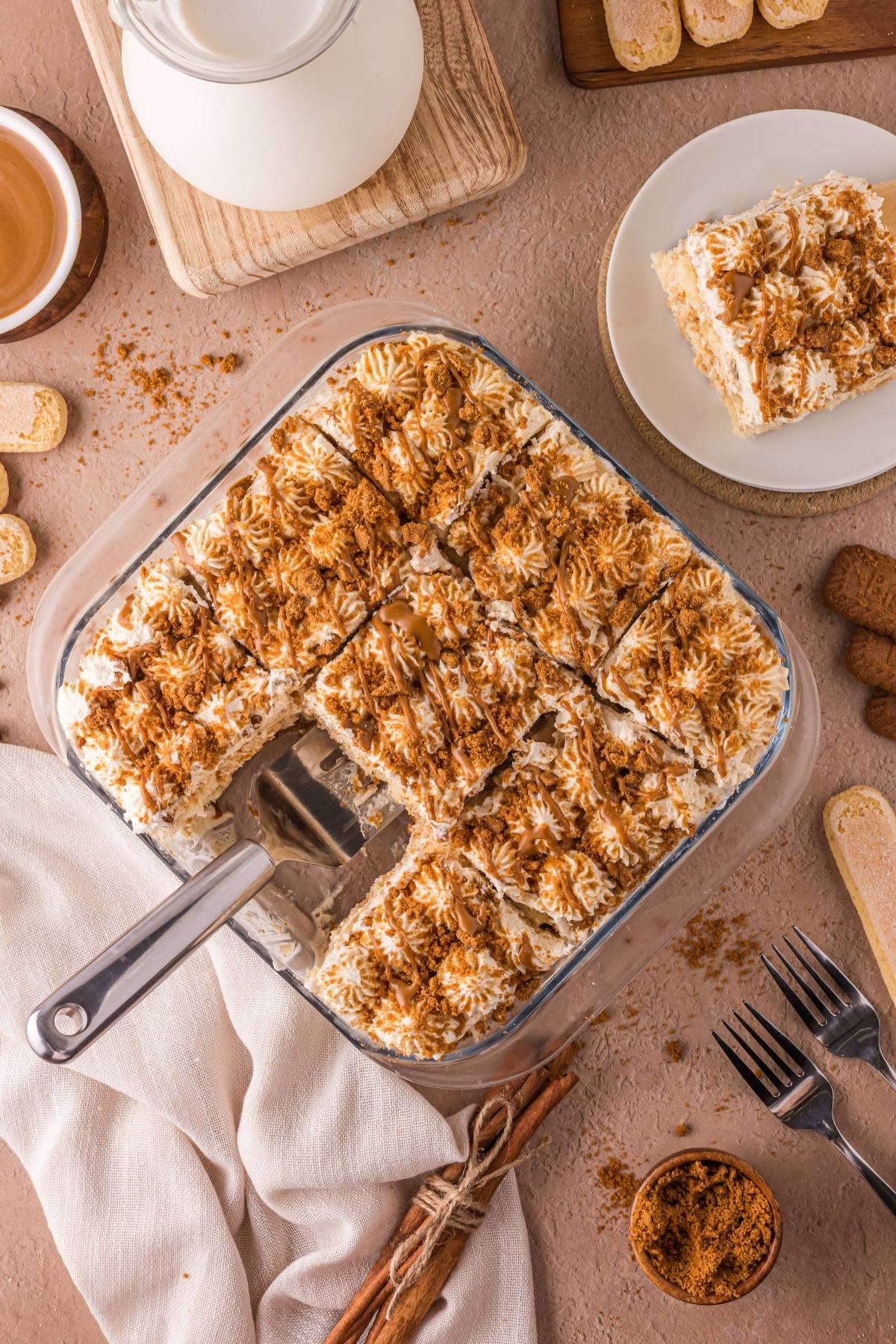 Top view of a sliced Biscoff tiramisu dessert in a glass dish with a serving spatula and one slice on a plate.