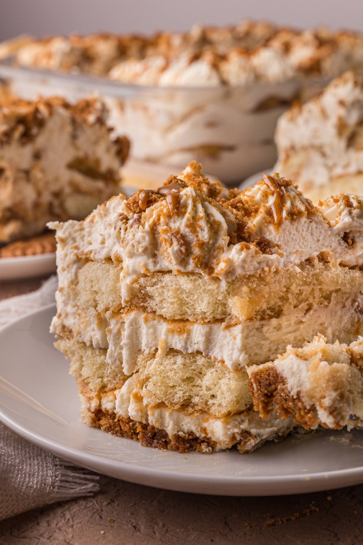A close-up of a creamy layered Biscoff  tiramisu dessert on a plate with more in the background.