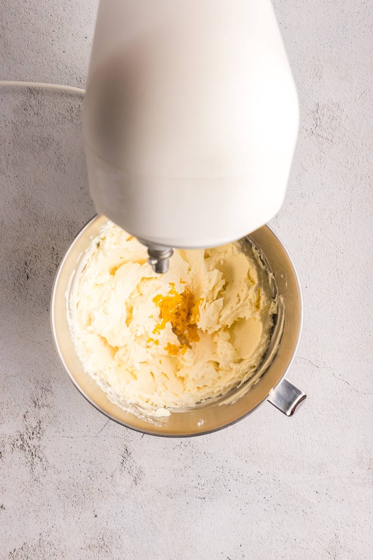 Overhead view of an electric mixer creaming ingredients with lemon zest in a metal mixing bowl.