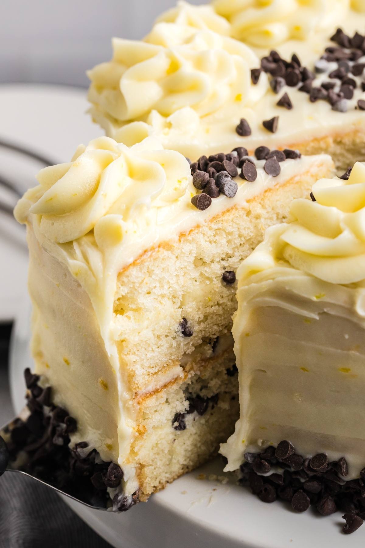 A slice of vanilla  Cannoli cake with chocolate chips and creamy frosting, topped with chocolate chips and frosting swirls.