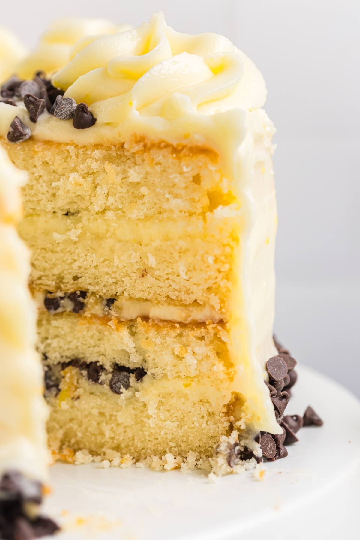 A three-layer vanilla  Cannoli cake with white frosting and chocolate chips, with one slice missing.