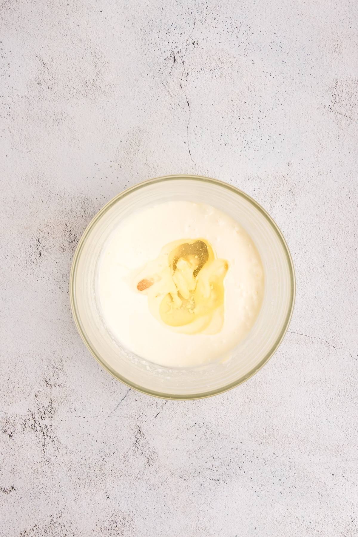 A bowl of white creamy mixture with a dollop of yellow substance on a light textured surface.