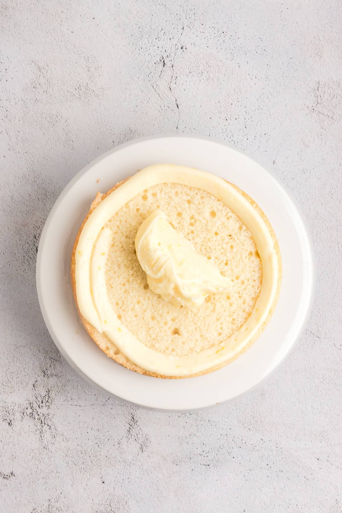 Round cake layer on a white plate, with a ring of frosting and a dollop of filling in the center.