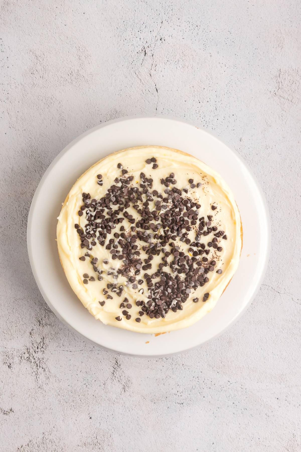 A round cheesecake topped with chocolate chips on a white plate against a light gray background.