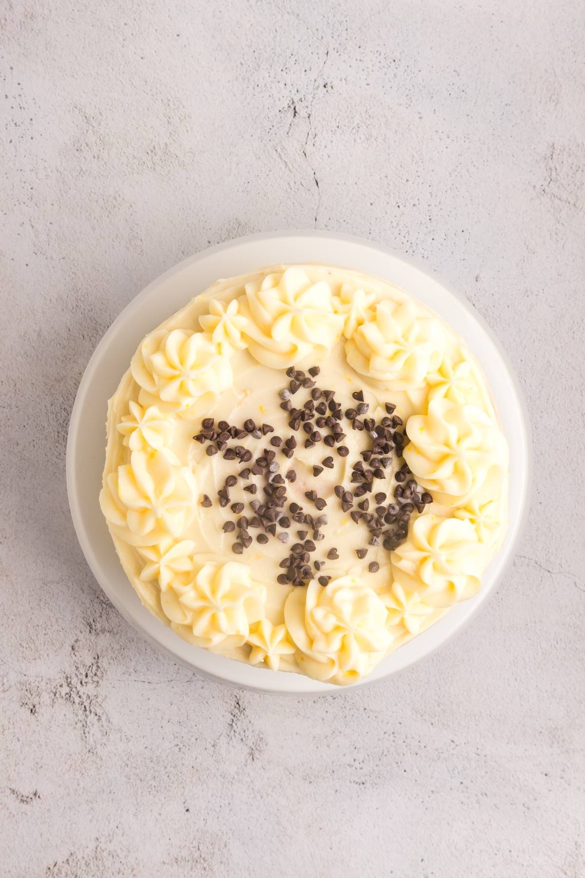 Round cake with white frosting, piped swirls, and chocolate chips in the center on a light gray surface.