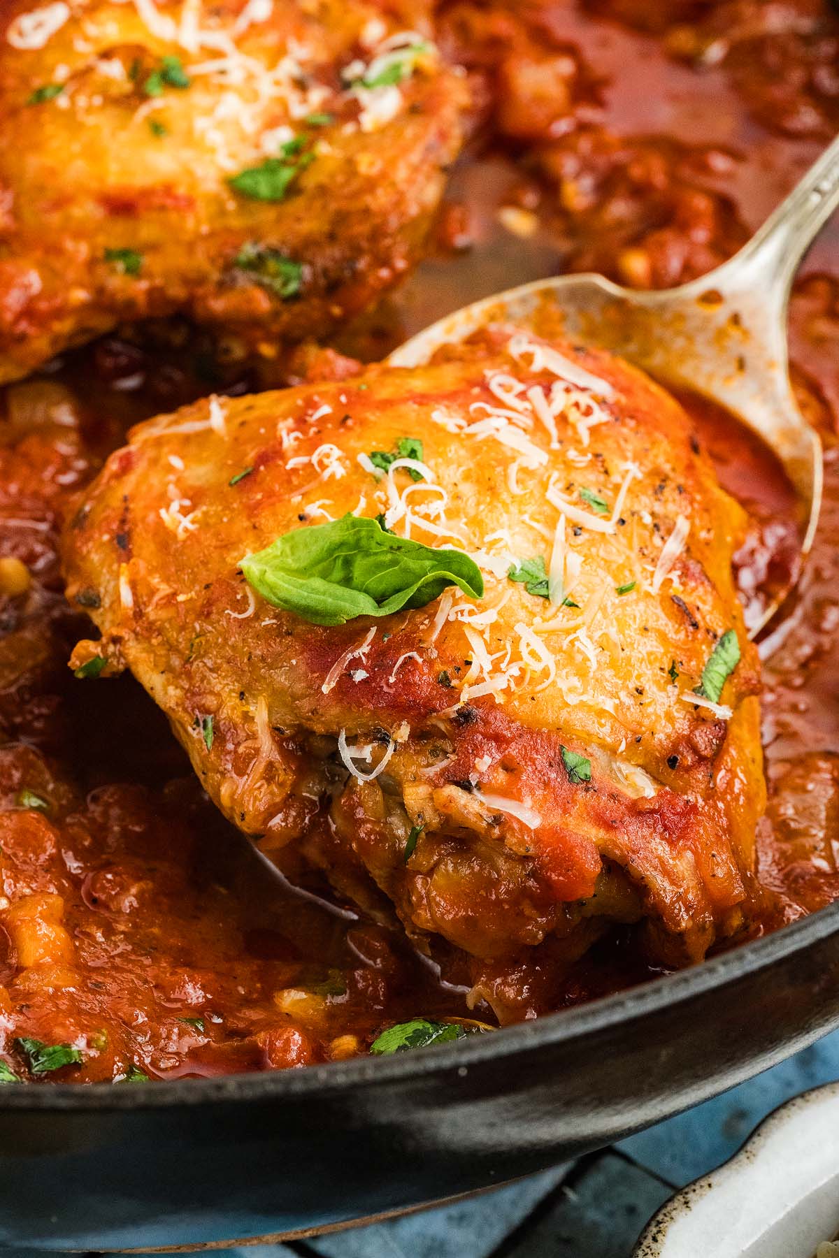 Close-up of chicken fra diavolo baked in tomato sauce, topped with herbs and grated cheese in a skillet.