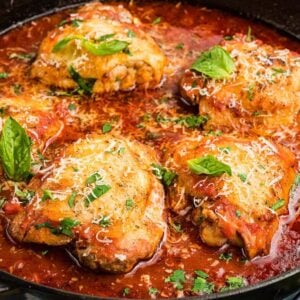 Chicken fra diavolo thighs simmered in zesty tomato sauce, garnished with fresh herbs and cheese, cooked to perfection in a black skillet.