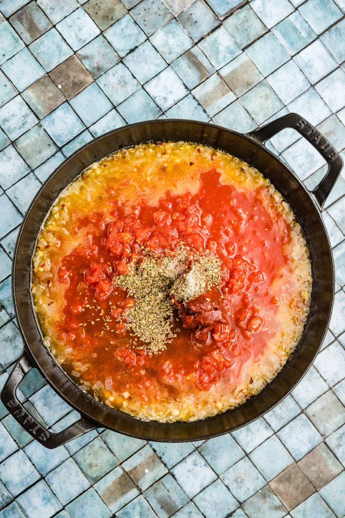 A pot of tomato sauce with herbs and spices on a blue tiled surface, seen from above.