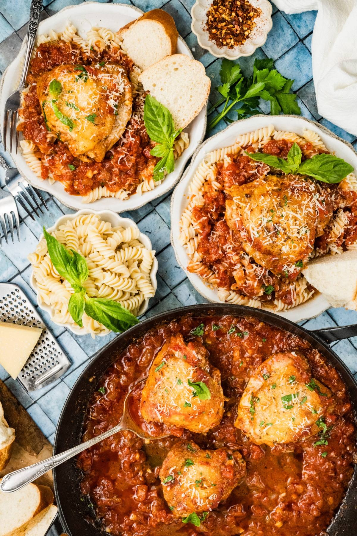Plates of pasta topped with Chicken fra diavolo in tomato sauce, garnished with herbs and served with bread slices.