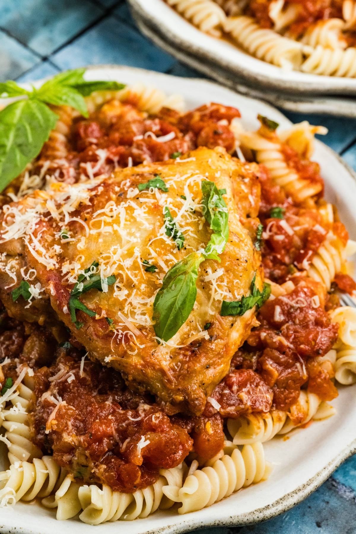 Cooked rotini pasta topped with tomato sauce, a piece of Chicken fra diavolo grated cheese, and fresh basil leaves.