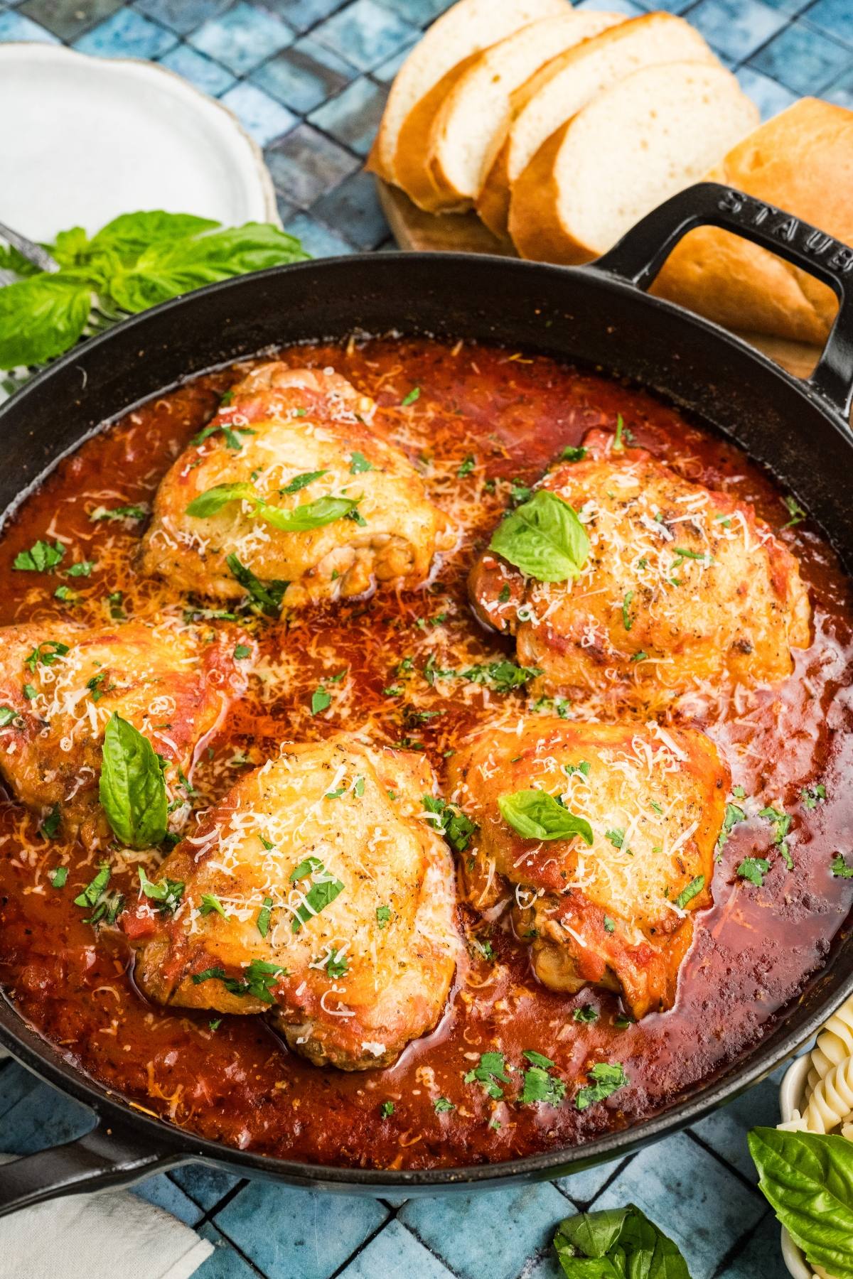Chicken fra diavolo thighs in tomato sauce, garnished with herbs and cheese, in a skillet with bread slices on the side.