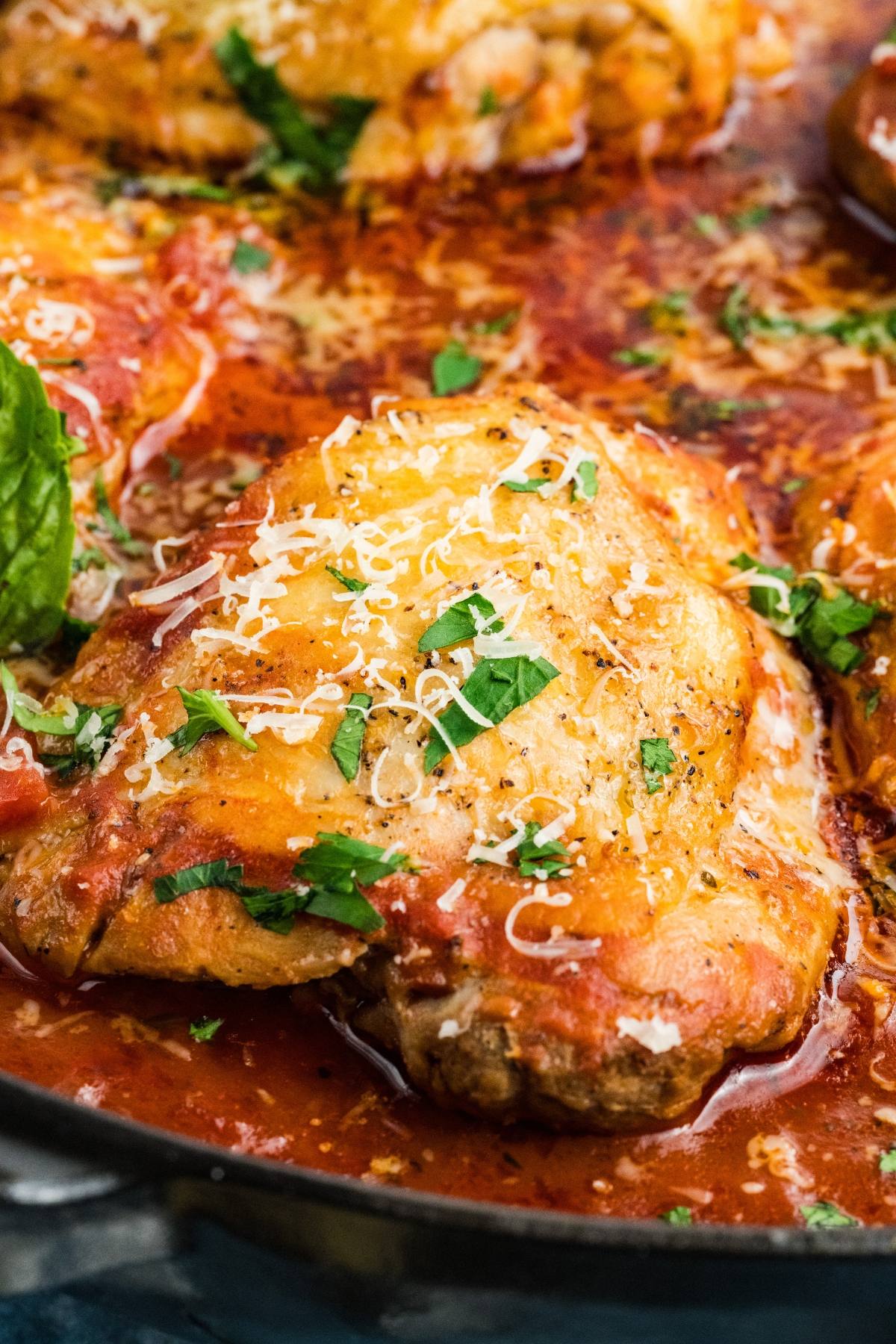 Chicken fra diavolo Parmesan topped with melted cheese and fresh herbs in a skillet with tomato sauce.