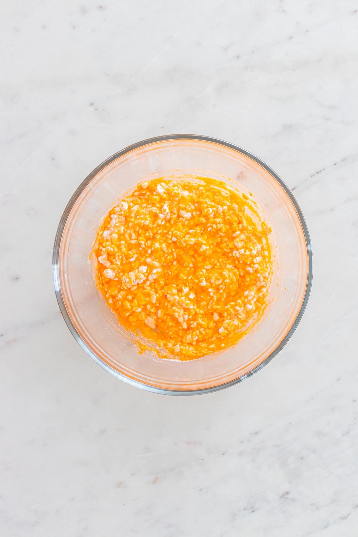 A glass bowl with a mixture of beaten eggs and sugar on a white marble surface.