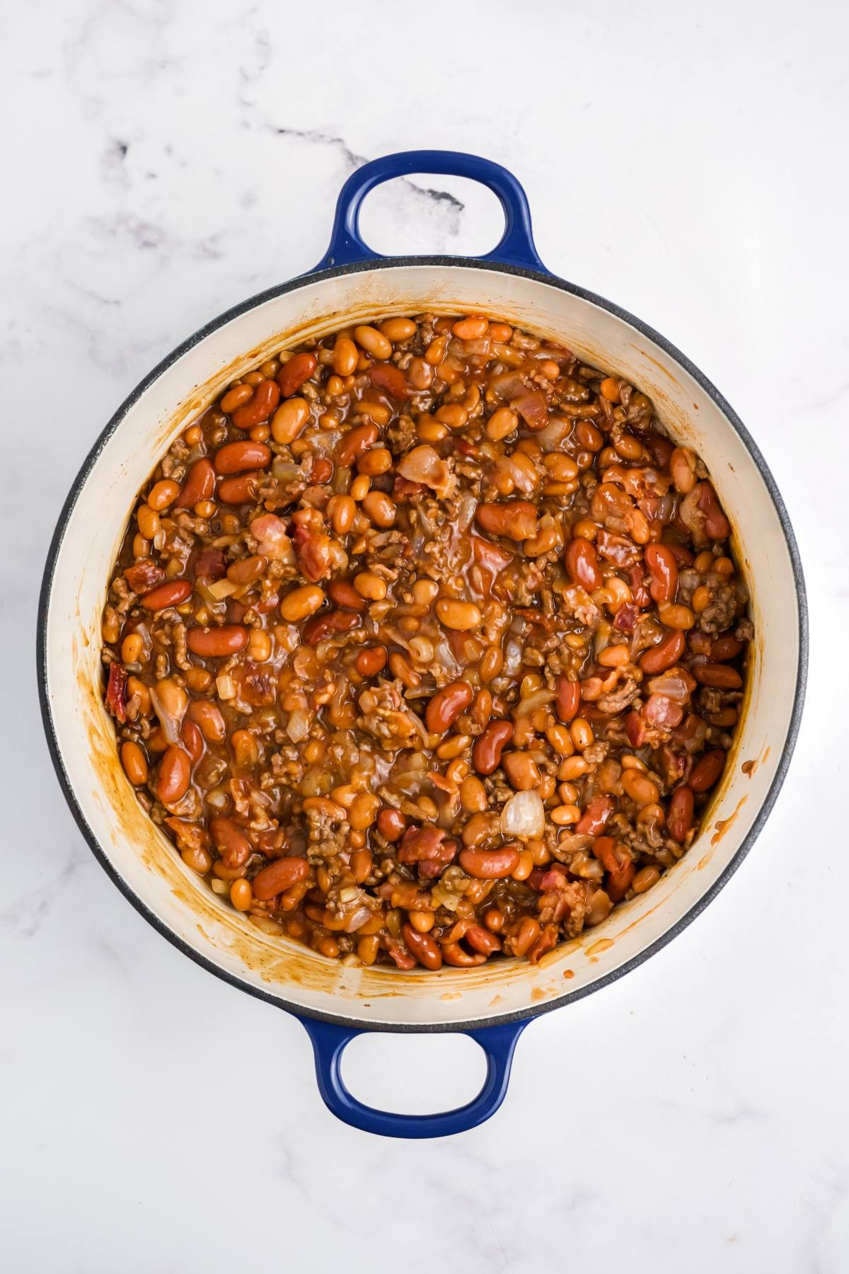 A pot filled with baked beans, ground beef, and sauce on a white marble surface.