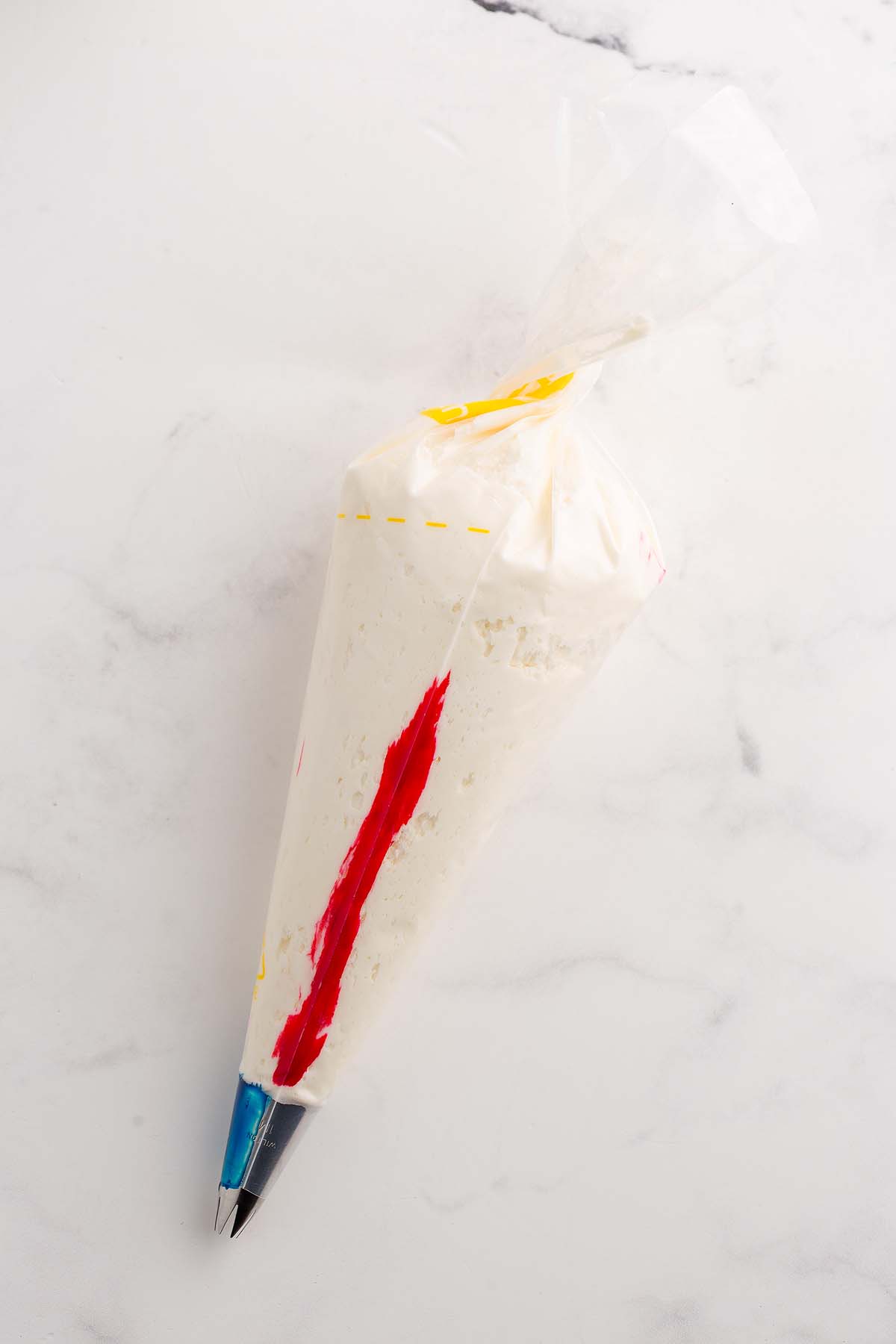 A piping bag filled with white frosting and a stripe of red color, fitted with a metal decorating tip&mdash;perfect for decorating gender reveal cupcakes.