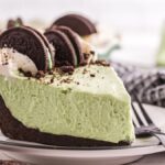 A slice of grasshopper pie with whipped cream and chocolate sandwich cookies sits on a plate with a fork.