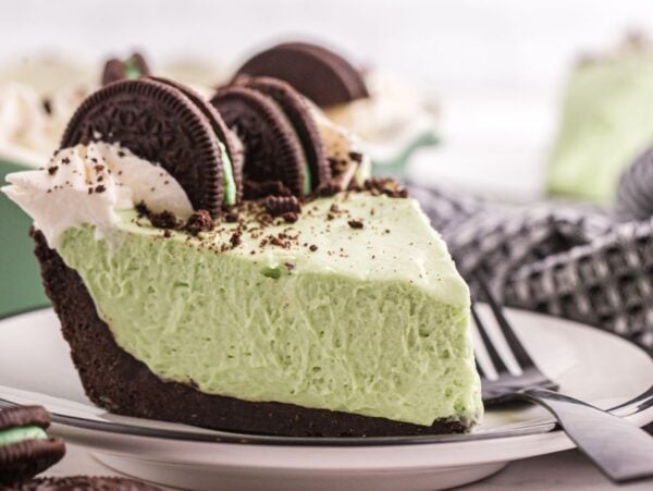 A slice of grasshopper pie with whipped cream and chocolate sandwich cookies sits on a plate with a fork.