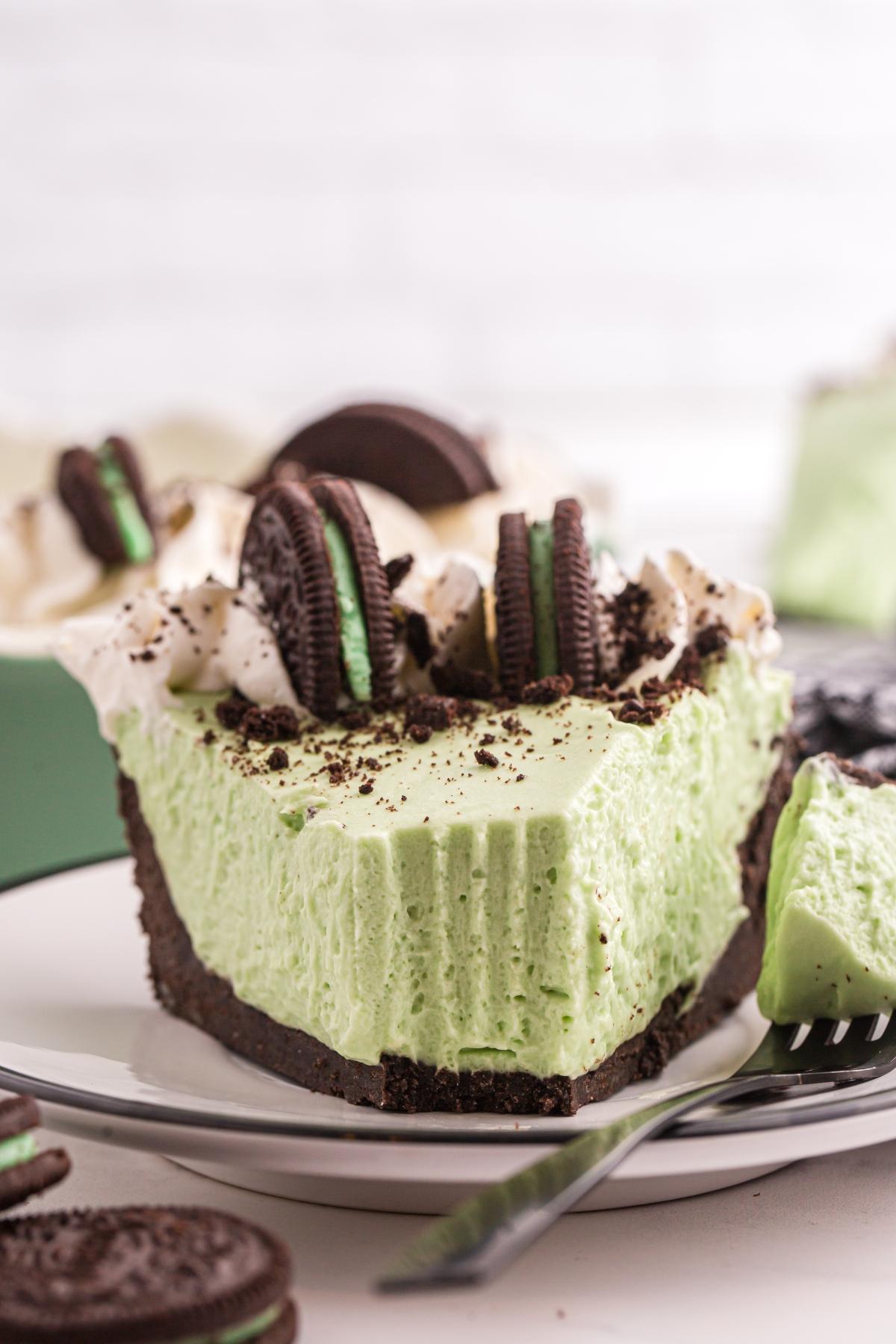 A slice of grasshopper pie with whipped topping and Oreo cookies on a plate, with a bite taken out.