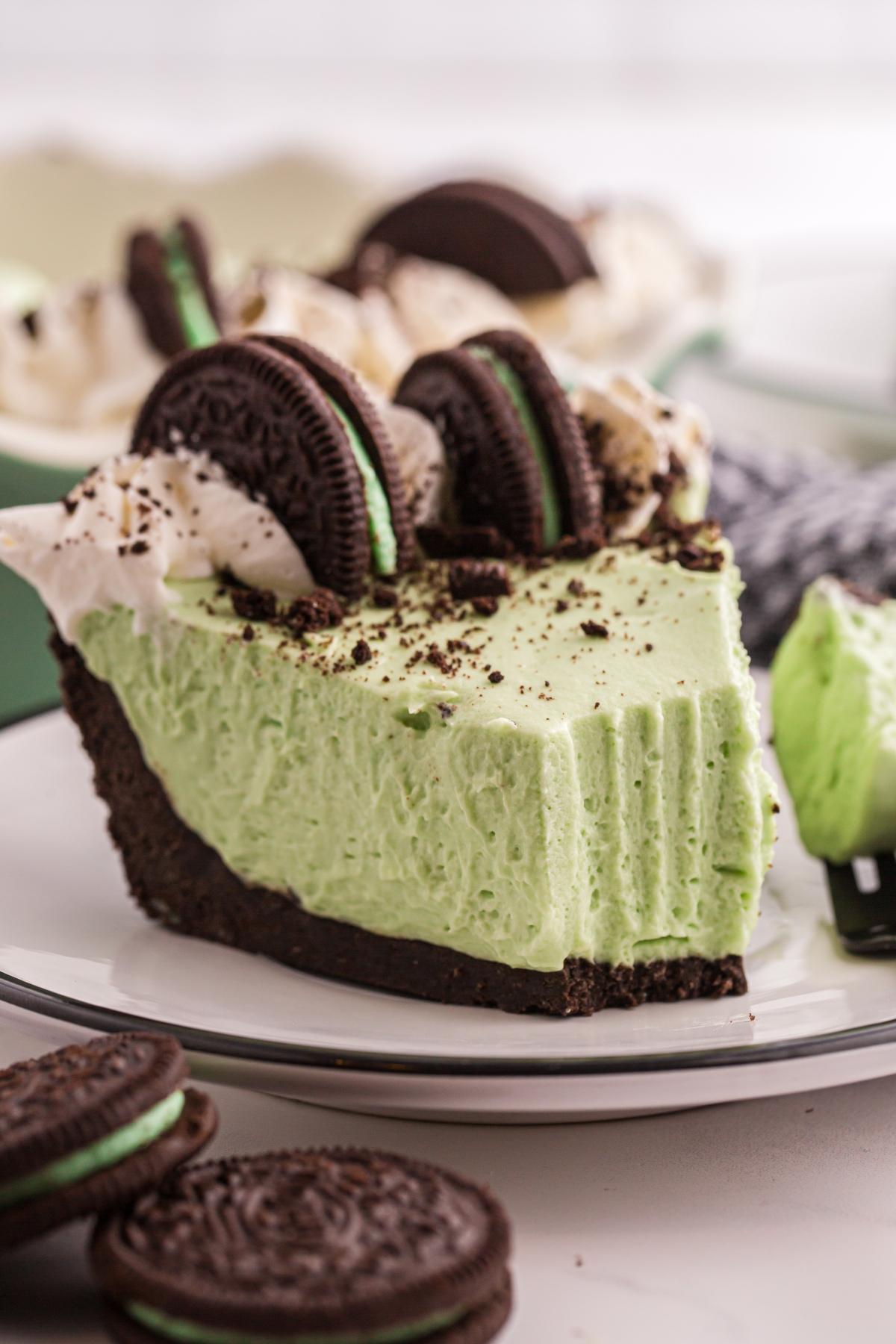 A slice of grasshopper pie with chocolate cookie crust, topped with whipped cream and chocolate sandwich cookies.