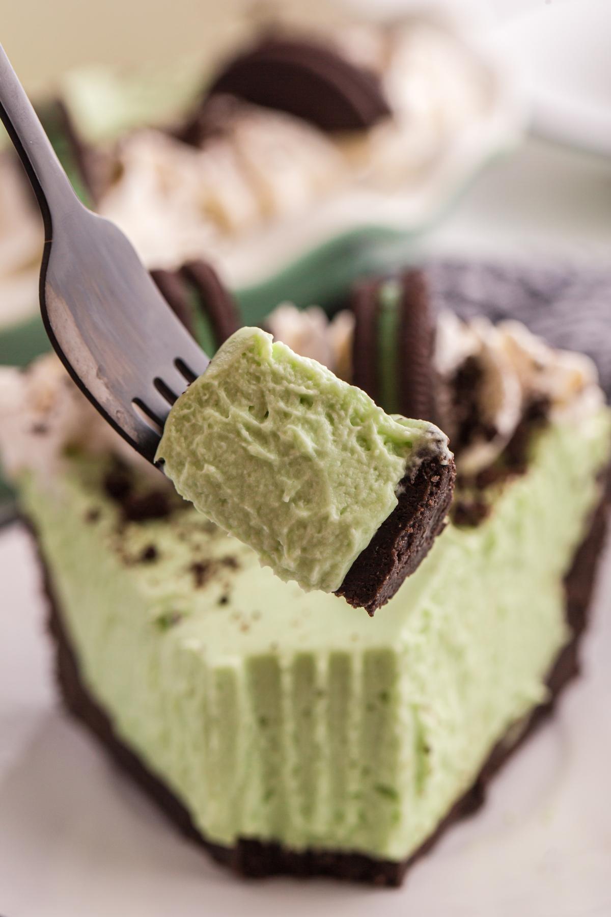 A fork holds a bite of creamy grasshopper pie with a chocolate crust and cookie topping.