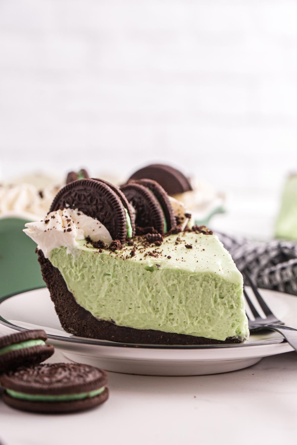 A slice of grasshopper pie with chocolate crust, topped with whipped cream and chocolate sandwich cookies.