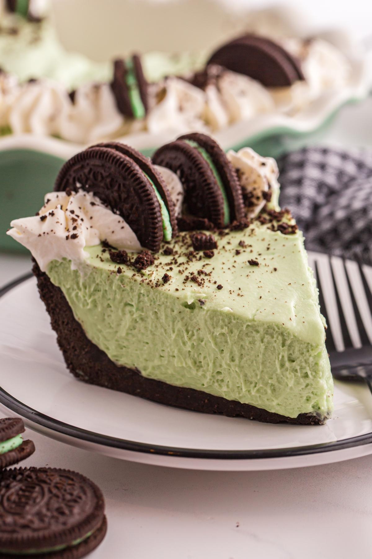 A slice of grasshopper pie with an Oreo crust, topped with whipped cream and Oreo cookies on a white plate.