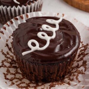 Chocolate cupcake with glossy frosting and a white icing swirl, sitting in an open paper liner next to a red napkin—just like classic Homemade Hostess Cupcakes.