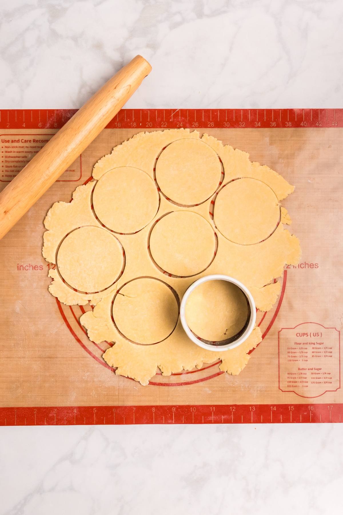 Round dough shapes cut with a biscuit cutter on a silicone mat, with a rolling pin nearby.